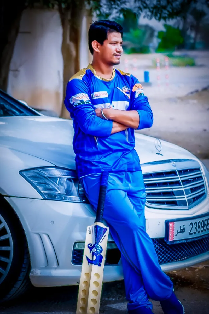 Habib in a blue jersey leaning on a car with a cricket bat